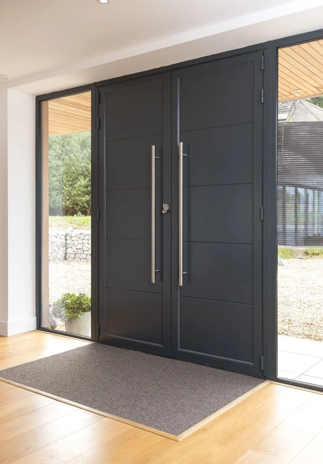 Black aluminium double doors with horizontal groove panels and brushed-steel bar handles viewed from a bright interior