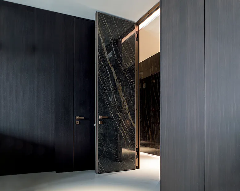 Black marble-effect aluminium pivot door ajar viewed from a dark panelled hallway