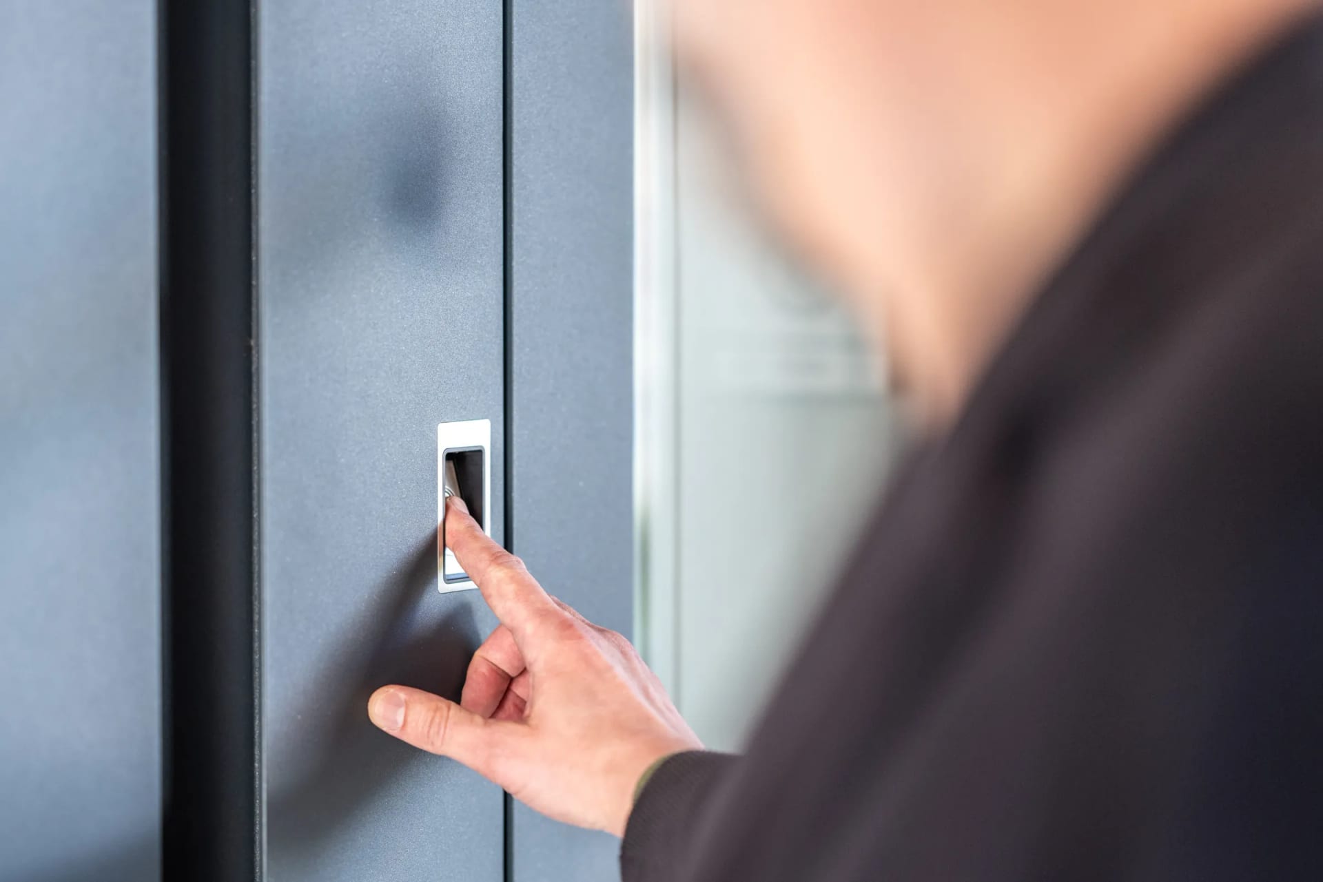 A hand pressing a recessed fingerprint reader on an aluminium door