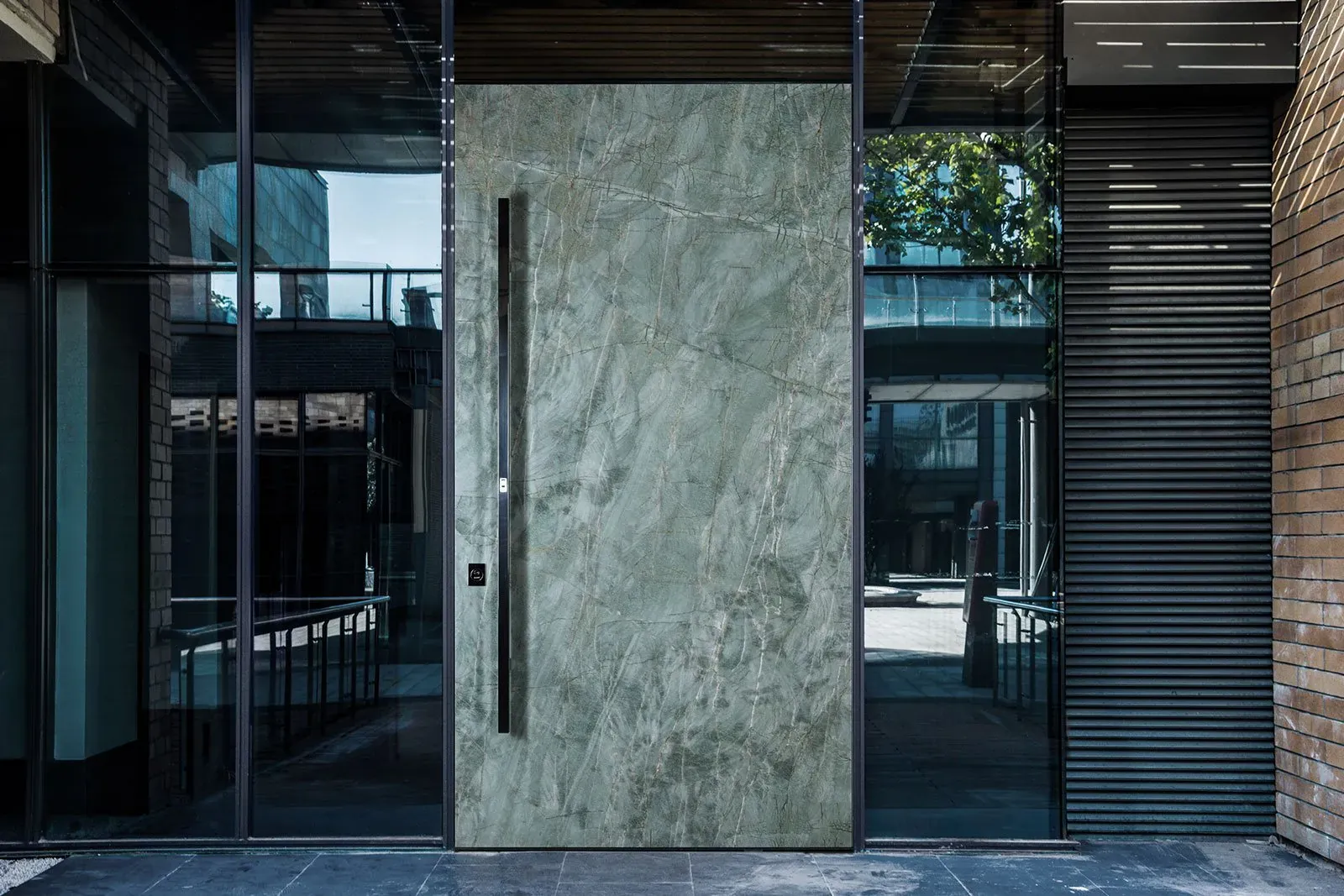 Green marble-effect pivot front door with a full-height bar handle in a glazed urban entrance