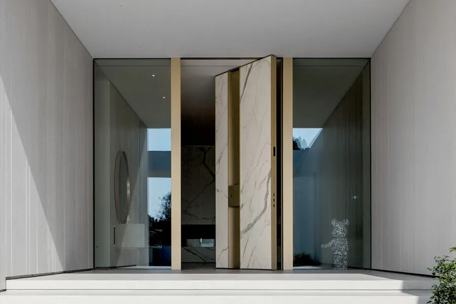 Calacatta-look marble pivot door set within a brushed-brass surround